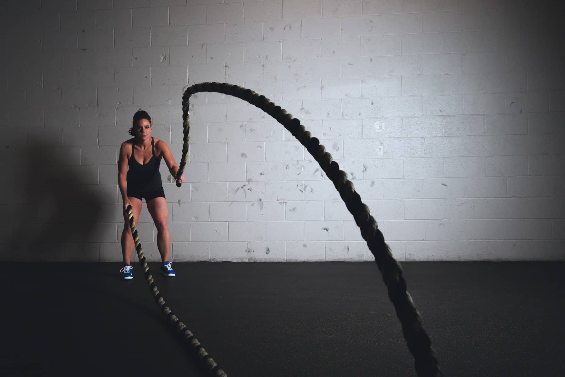 Athletic woman in black singlet and shorts training in a gym with heavy ropes